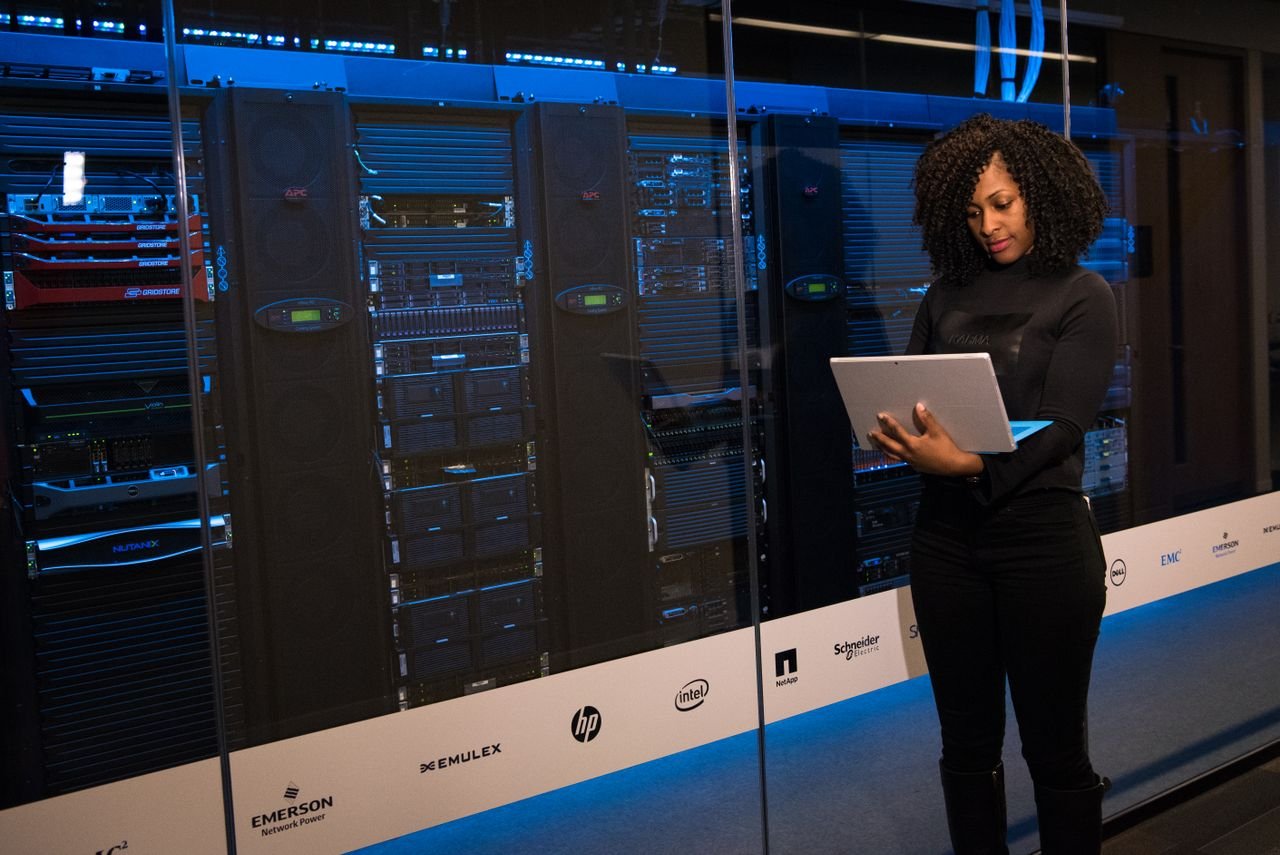 about-bg A female engineer using a laptop while monitoring data servers in a modern server room.