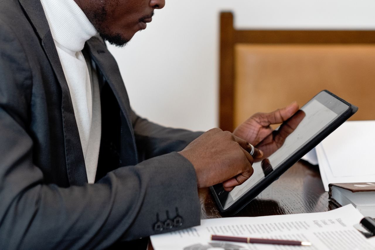 who-we-are A businessman in a suit uses a tablet at a desk, focusing on technology for productivity.
